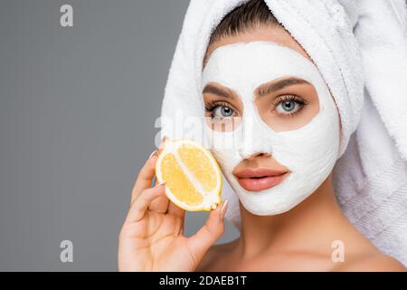 femme avec une serviette sur la tête et un masque en argile sur le visage tenir le citron isolé sur le gris Banque D'Images