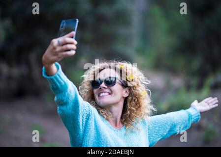 Bonne femme de race blanche adulte qui profite du téléphone pour prendre des photos pour partager sur les médias sociaux - activités de loisirs en plein air et forêt verte en arrière-plan Banque D'Images