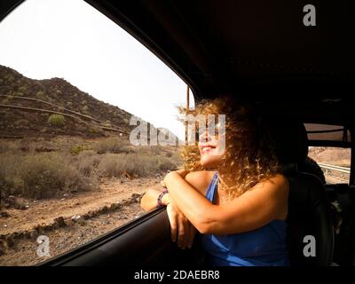 Joyeux et heureux adulte belle femme appréciant le voyage comme voiture passager - cheveux et vent pour le voyage et la liberté Concept - montagnes et paysages extérieurs à l'extérieur du véhicule Banque D'Images