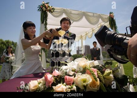 BEIJING, CHINE - JUIN 2006: Yang Ying, 26 ans, un employé de banque, et sa mariée Xu Wei, 26 ans qui travaille dans I.T. remplir une pyramide de verres de champagne à ne pas Banque D'Images