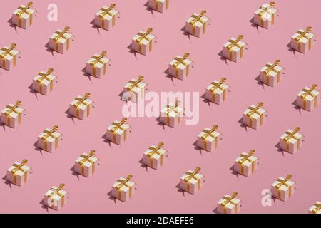 Motif de boîtes-cadeaux blanches avec noeud en ruban doré sur fond rose. Style minimaliste. Cadeaux d'anniversaire ou de Noël. Banque D'Images