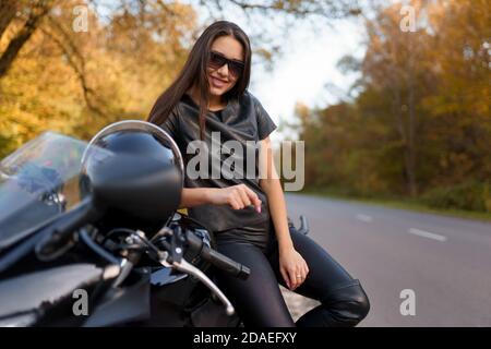 Belle femme motocycliste en lunettes et des vêtements en cuir noir est assis sur vélo de sport Banque D'Images