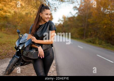 Une motard femelle se tient près de la moto sur le bord de la route et tient un casque Banque D'Images