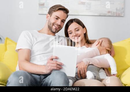 tablette numérique dans la main de l'homme près de la bonne femme tenant dans les bras bébé fils Banque D'Images