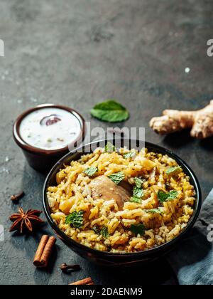 Cuisine pakistanaise - riz biryani avec poulet et sauce au yaourt à la raita. Délicieux poulet à base d'hyberabadi biryani sur fond noir. Copier l'espace pour le texte. Verticale Banque D'Images