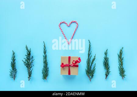 Le cadeau du nouvel an, des tours de cyprès et un coeur fait de deux cannes de bonbons sur fond bleu. Mise en page de Noël, mise en page à plat, espace de copie. Banque D'Images