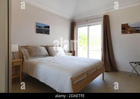 Chambre double moderne et propre avec portes coulissantes en verre, literie blanche et cadre de lit en bois Banque D'Images