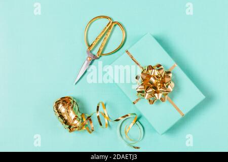 Vue de dessus du processus d'emballage des cadeaux avec boîte, ruban doré et ciseaux sur fond bleu. Banque D'Images