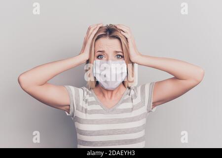 Gros plan d'une femme contrariée tenant la tête avec les mains port d'un masque blanc isolé sur fond gris Banque D'Images