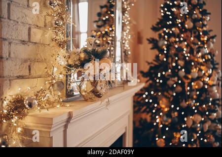 Cheminée classique blanche avec décorations du nouvel an sur fond d'arbre décoré de Noël avec des guirlandes étincelantes. Fragment de l'intérieur du salon de fête du nouvel an la nuit Banque D'Images