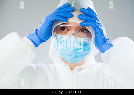 Travailleur médical désespéré NHS EMS en costume blanc de protection, bleu chirurgical Masque gants en latex et lunettes de sécurité, coronavirus COVID-19 crise pandémique Banque D'Images