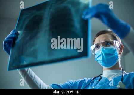 Pneumologue ou oncologue féminin tenant un examen de radiographie thoracique, inspectant le patient COVID-19 Poumons, port d'un EPI uniforme, coronavirus virus respiratoire aigu Banque D'Images