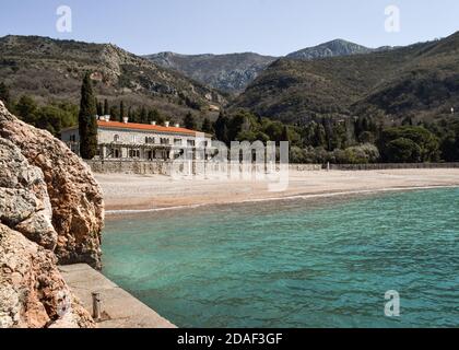 QUEEN'S BEACH, SVETI STEFAN, MONTÉNÉGRO - 25 MARS 2016 : rochers, mer bleue arrivant sur la plage de gravier, montagnes et Villa Milocer, bâtiment de deux étages Banque D'Images