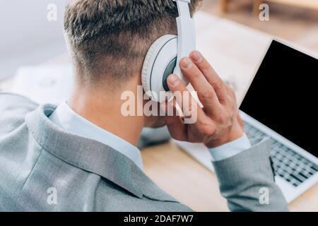 Vue arrière d'un homme d'affaires touchant un casque tout en utilisant un ordinateur portable arrière-plan flou Banque D'Images