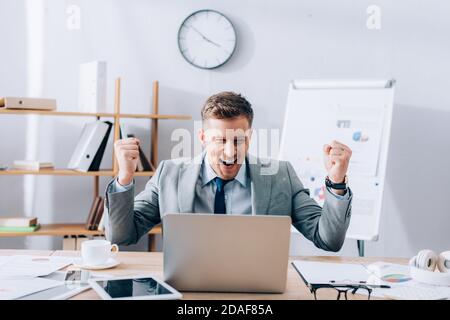 Homme d'affaires souriant montrant un geste près d'un ordinateur portable et de ses papiers tableau Banque D'Images