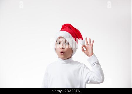 Le garçon dans un chapeau de père Noël rouge montre un geste de 'ok'. Concept de Noël. Banque D'Images