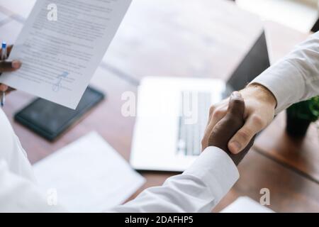 Vue de dessus de la poignée de main de l'homme d'affaires africain et de l'homme d'affaires caucasien sur le lieu de travail, gros plan. Banque D'Images