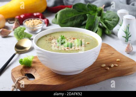 Soupe à la crème végétarienne au brocoli, aux épinards et aux courgettes dans un bol blanc sur fond gris. Gros plan. Banque D'Images