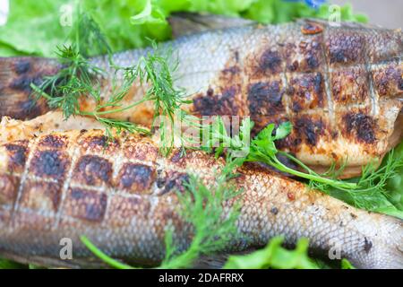 Poisson frit au bar sur un grill avec des légumes verts Banque D'Images