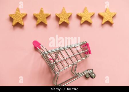 Simple Flat Lay design petit supermarché pousser chariot pour le shopping et 5 étoiles d'or isolées sur fond rose pastel. Concept d'évaluation et de révision en ligne des achats de produits de consommation au détail Banque D'Images