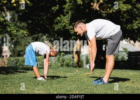 Homme et garçon dans des vêtements de sport avec des mains tendues, penché vers l'avant dans le parc avec arbres flous sur l'arrière-plan Banque D'Images