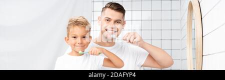 Fils souriants et père tenant des brosses à dents et regardant l'appareil photo, la bannière Banque D'Images