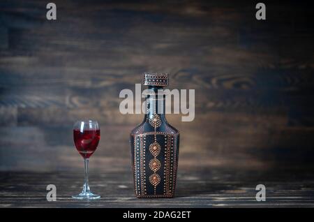 Teinture maison de cerise rouge dans des bouteilles décoratives et un verre de vin sur fond de bois, Ukraine, gros plan Banque D'Images