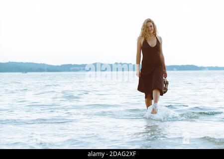 Woman in Black Robe de lumière marche pieds nus par mer plage Banque D'Images