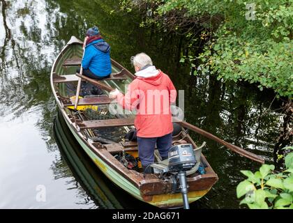 Retraités de couple aîné pagayant sur un bateau de pêche ou un bateau de clinker dans une petite crique de lac dans le parc national de Killarney, comté de Kerry, Irlande, Europe Banque D'Images