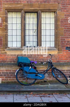 un vélo étudiant appuyé contre le mur d'un bâtiment historique ou d'une université dans la ville universitaire de cambridge sous une fenêtre. Banque D'Images