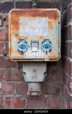 Prise électrique extérieure rouillée avec yeux sur le mur en brique rouge Banque D'Images