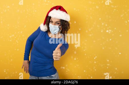 Femme avec chapeau de Noël est optimiste au sujet de la défaite de covid 19 coronavirus. Fond jaune. Banque D'Images