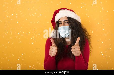 Femme avec chapeau de Noël est optimiste au sujet de la défaite de covid 19 coronavirus. Fond jaune. Banque D'Images