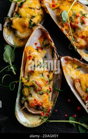 moules cuites au four avec du fromage et des légumes sur fond noir Banque D'Images