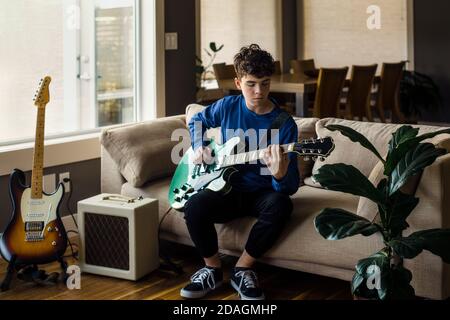 Jeune musicien masculin jouant de la guitare électrique à la maison Banque D'Images