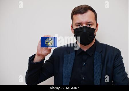 Homme porter noir formel et protéger masque, tenir la carte drapeau Nebraska isolée sur fond blanc. USA coronavirus Covid pays concept. Banque D'Images