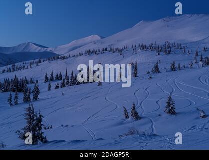 Remontée mécanique de la station de ski alpin avec sièges qui passent au-dessus des pistes de ski de montagne avant le lever du soleil et des bosquets de sapins. Svydovets vue de la crête depuis le glissement Banque D'Images