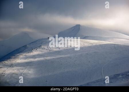 Piste de montagne enneigée en plein soleil le soir dernier. Magnifique crépuscule venteux sur la pittoresque station de ski alpin, Dragobrat, Ukraine, Carpates Mountain Banque D'Images