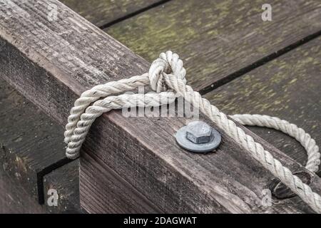 Une corde blanche à trois brins, fixant un bateau, est enroulée autour d'un rail à taureau d'un quai en bois brun et abîmé sur la côte ouest du Canada (bateau non visible). Banque D'Images