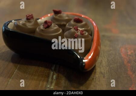 Pralines au chocolat, nappées de framboise, servies en forme de cœur bol sur une table en bois Banque D'Images