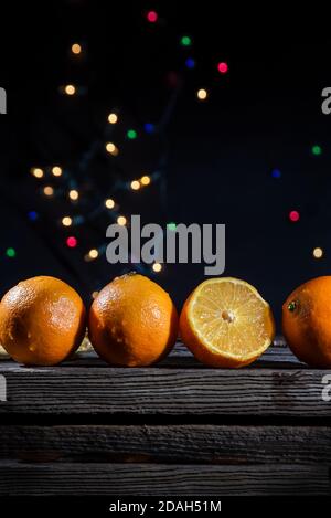 Une rangée de quatre oranges clémentines sur un bois de grange carte avec des lumières de fond sur fond noir Banque D'Images