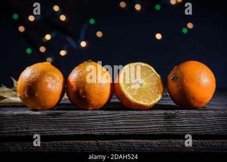 Une rangée de quatre oranges clémentines sur un bois de grange carte avec des lumières de fond sur fond noir Banque D'Images