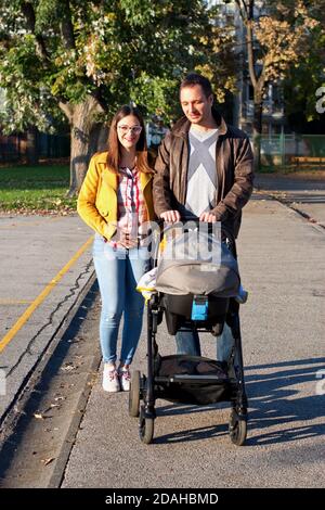 Jeune couple marchant dans le parc et poussant leur bébé dans poussette Banque D'Images