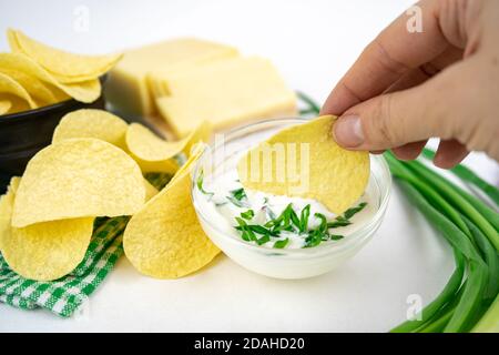 Prenez les frites d'un bol et trempez-les dans une sauce à la crème aigre à l'oignon vert. Banque D'Images