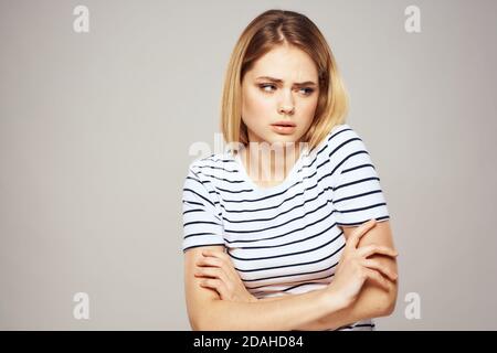 Une femme dans un T-shirt rayé tient ses mains dans face à ses émotions displaiser arrière-plan clair Banque D'Images