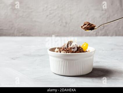 Mousse au chocolat garnie d'un coin de mandarine et de copeaux de chocolat blanc dans un bol blanc et une cuillère à café avec mousse au chocolat sur fond gris, co Banque D'Images