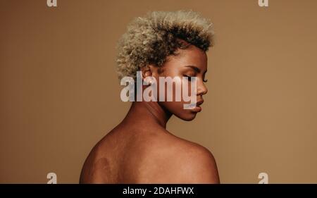 Gros plan sur une femme afro-américaine qui regarde par-dessus l'épaule. Portrait de la femme en cheveux bouclés sur fond marron. Banque D'Images