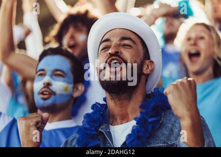 Foule de fans de football argentins acclamant leur équipe avec des guirlandes bleues et des drapeaux argentins au stade. fans de football assis au stade cheeri Banque D'Images