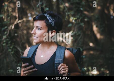 Portrait d'une belle femme tenant son téléphone dans le forêt pendant la randonnée avec un sac à dos Banque D'Images