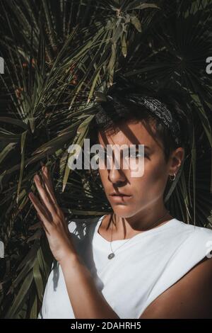 Portrait d'une belle femme à travers les feuilles de une plante qui regarde loin avec des feuilles vertes en arrière-plan et la lumière du soleil Banque D'Images